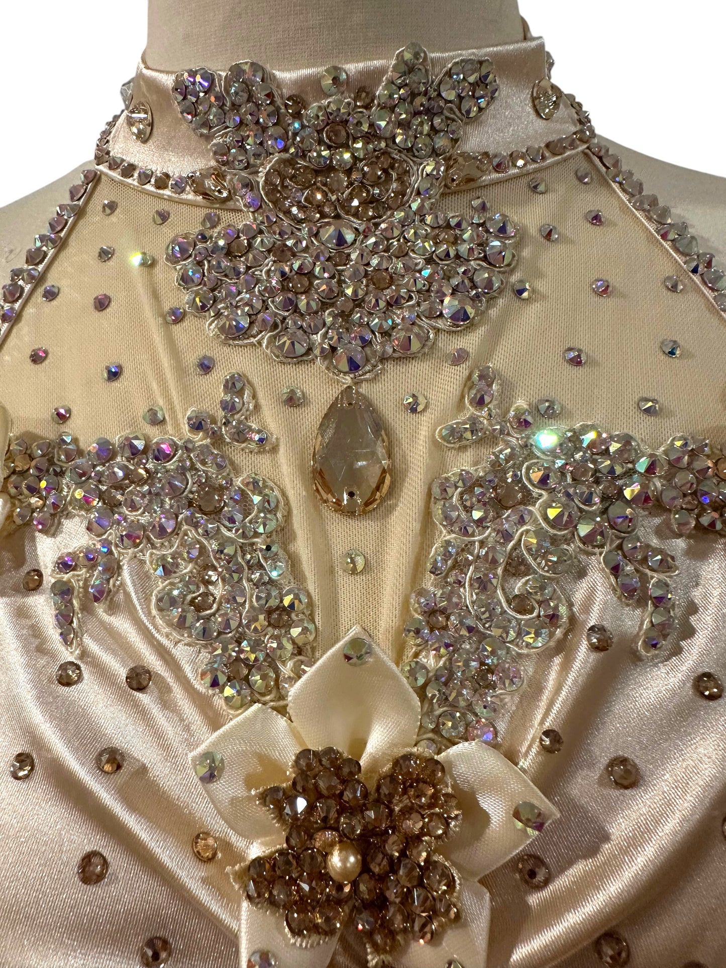 Close-up of the Aubrey dance costume bodice featuring hand-placed crystal appliqués, dimensional floral embellishments, illusion mesh, and almond white satin draping.