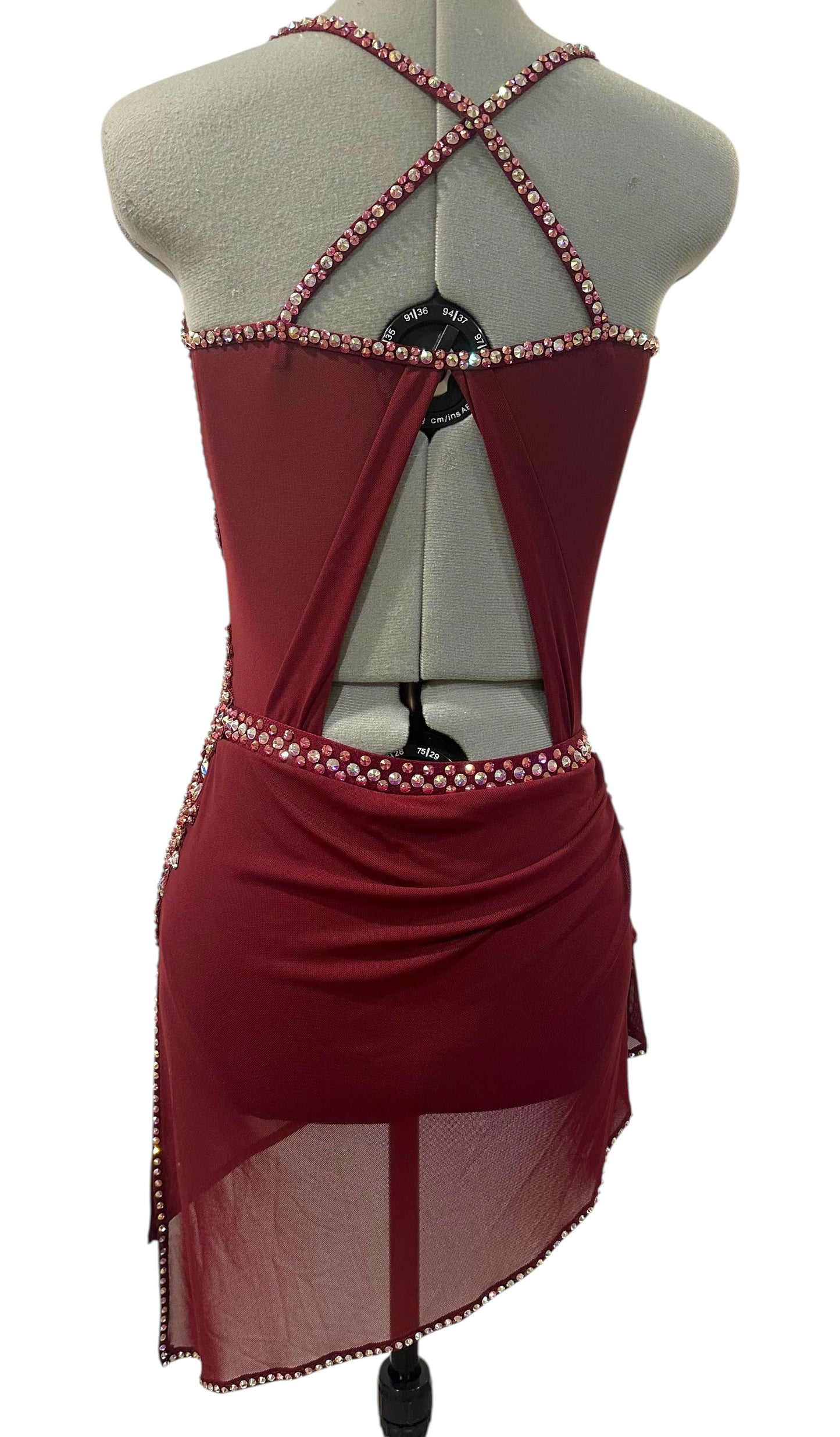 Back view of burgundy competition dance costume featuring crossed rhinestone straps, open back design, and asymmetrical skirt