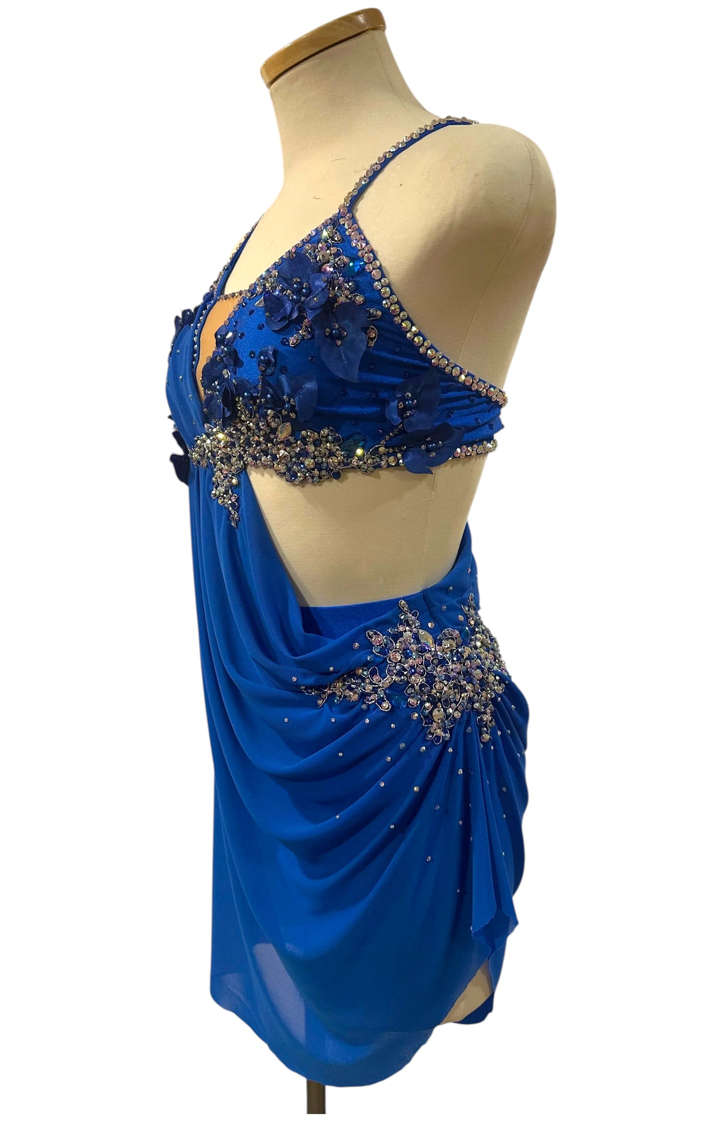 Front left angled view of royal blue competition dance costume with floral appliqués, rhinestones, and flowing chiffon draping.