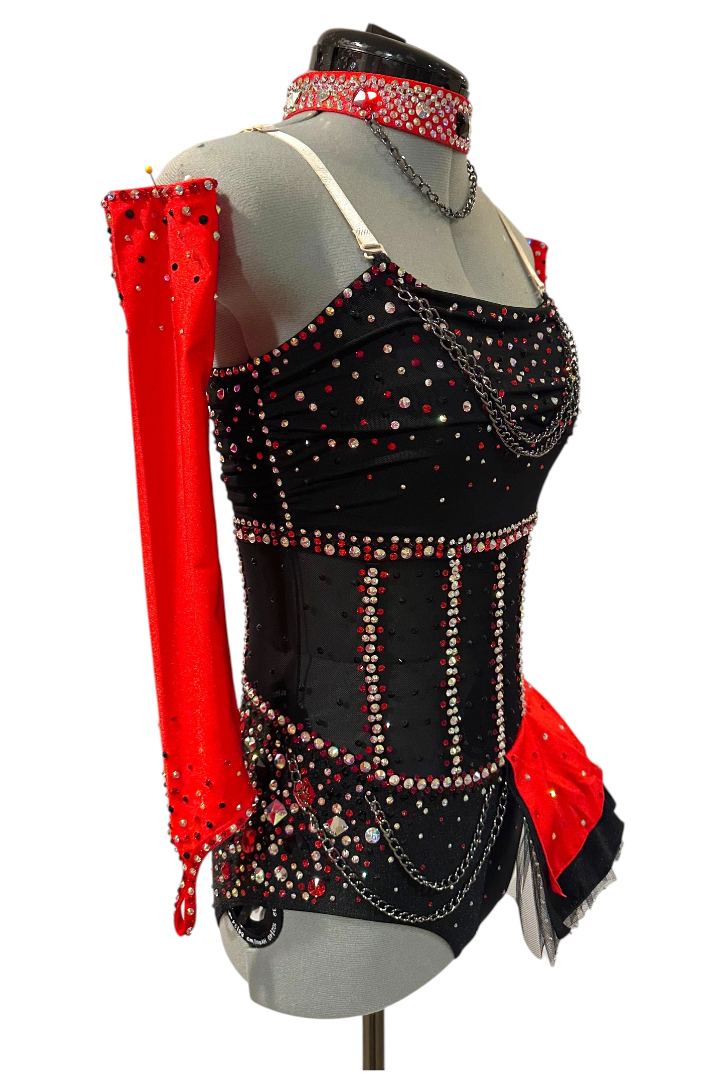 Side view of a black and red competition dance costume with an illusion mesh corset, layered chain details, detachable red sleeves, and rhinestone embellishments.