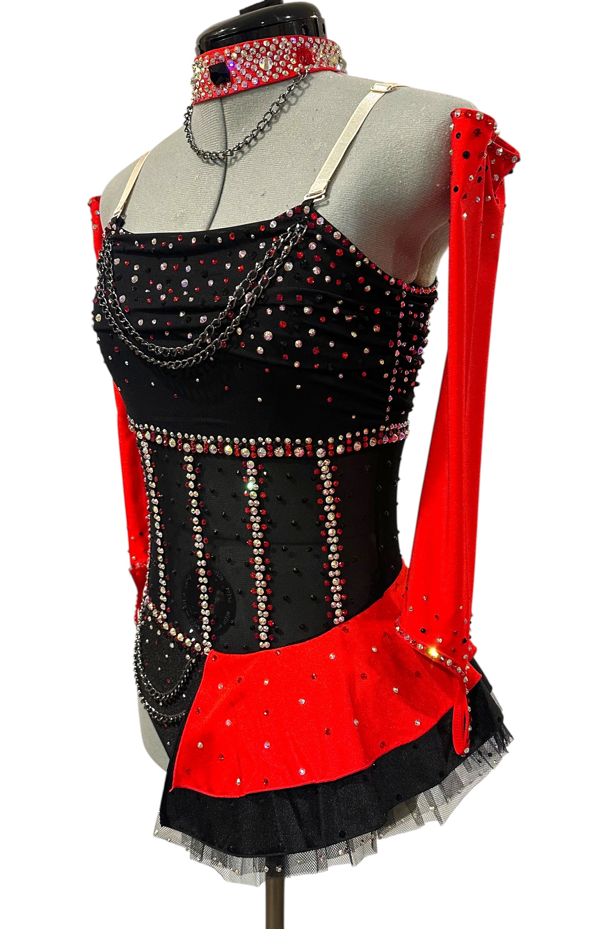 Left side view of a black and red competition dance costume with an illusion mesh corset, layered chain details, detachable red sleeves, and rhinestone embellishments.