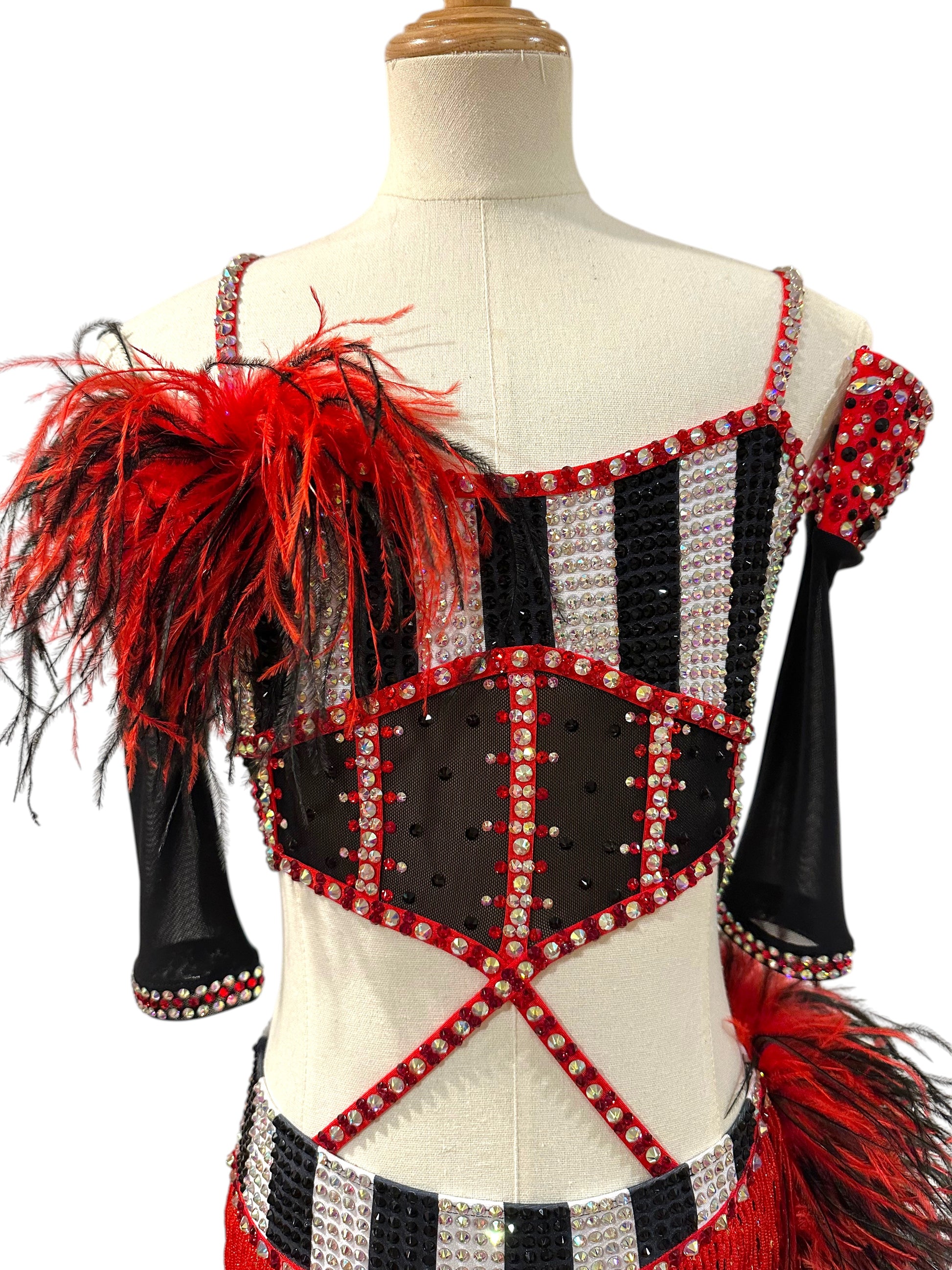 Close-up front view of a red, black and white rhinestone dance costume highlighting striped bodice, feather shoulder detail, and sparkling crystal embellishments.