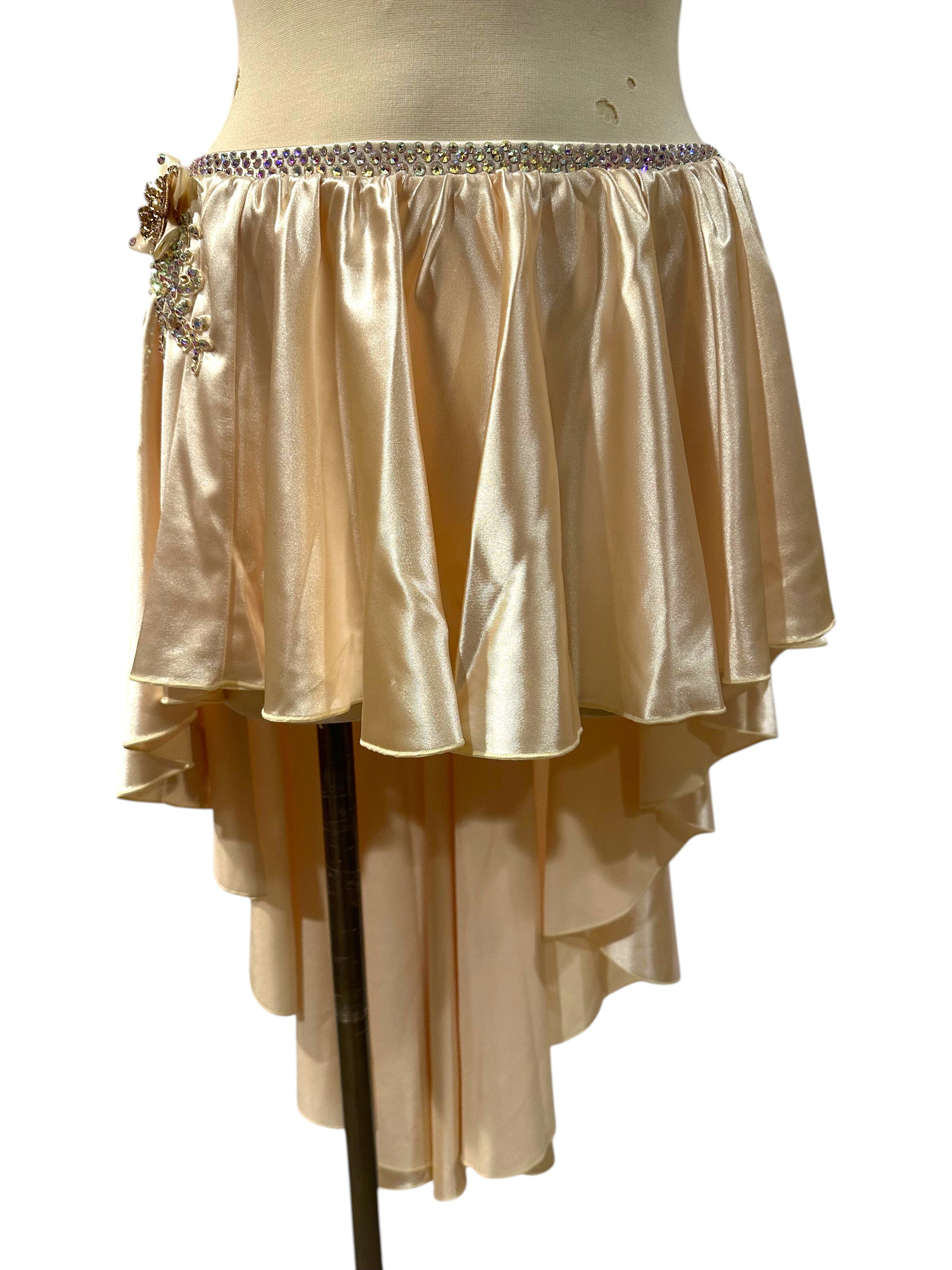 Close-up of the almond white satin asymmetrical dance skirt featuring layered satin panels, rhinestone waistband, and floral crystal appliqué detail.