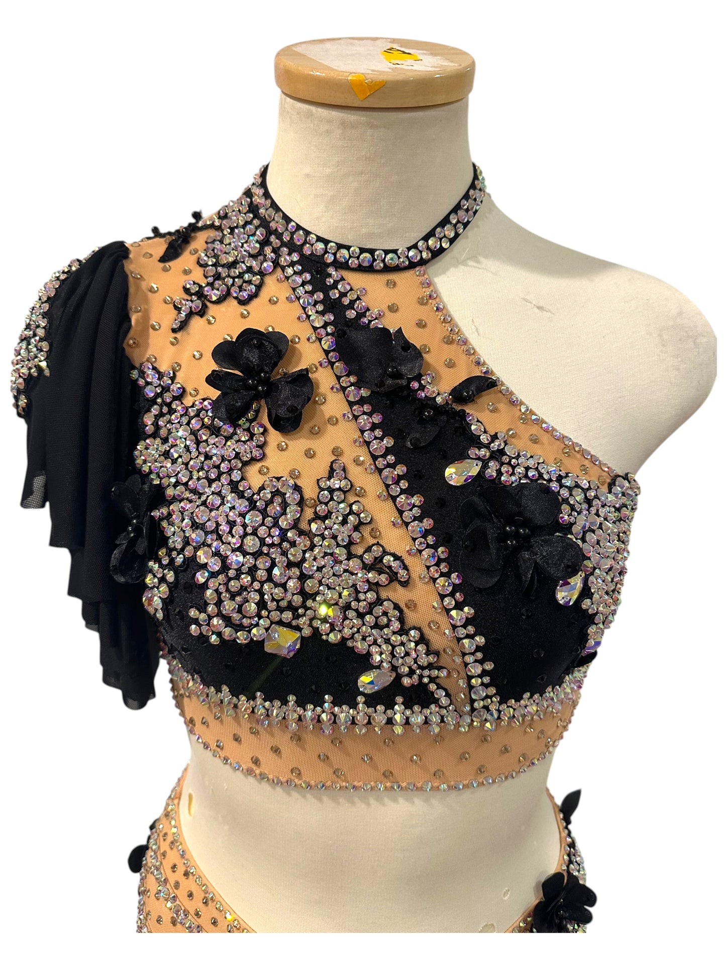 Close-up of Scarlett dance costume bodice with AB crystals, black floral appliqués, nude mesh, and one-shoulder design.