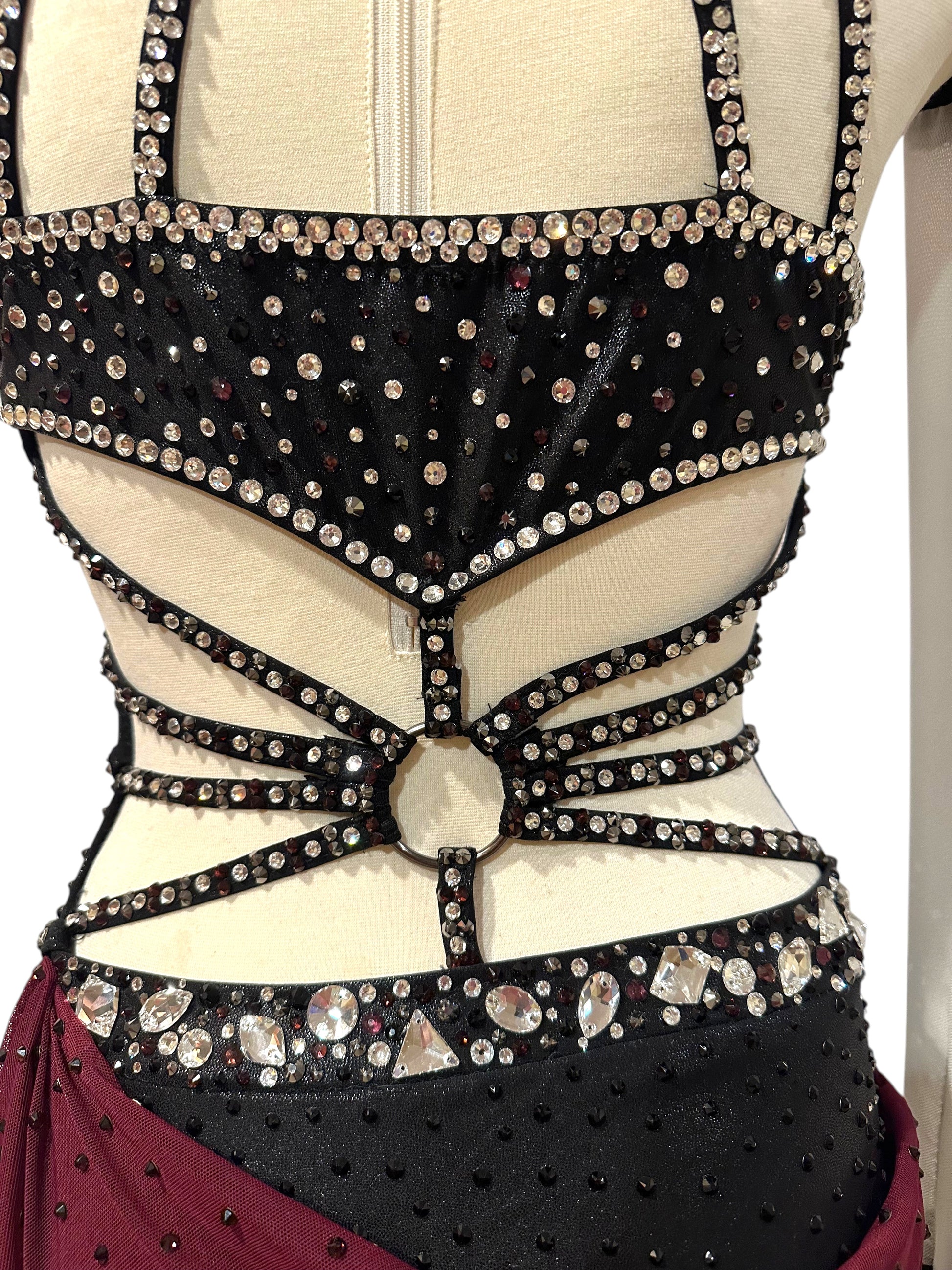 Close-up of open back on black dance costume with rhinestone-covered straps, center ring detail and crystal waistband.