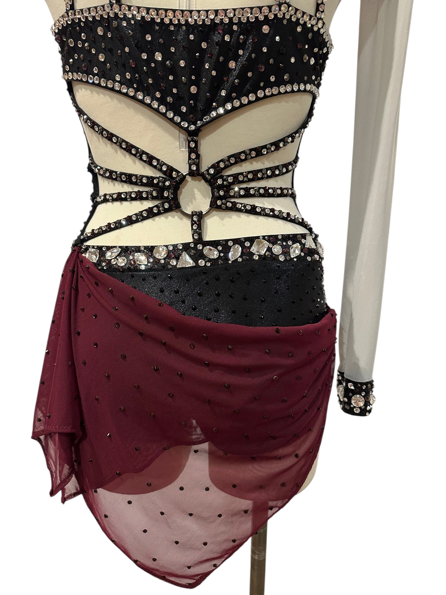 Lower back view of black and burgundy dance costume with crystal waistband, strappy detailing and asymmetrical burgundy mesh drape.