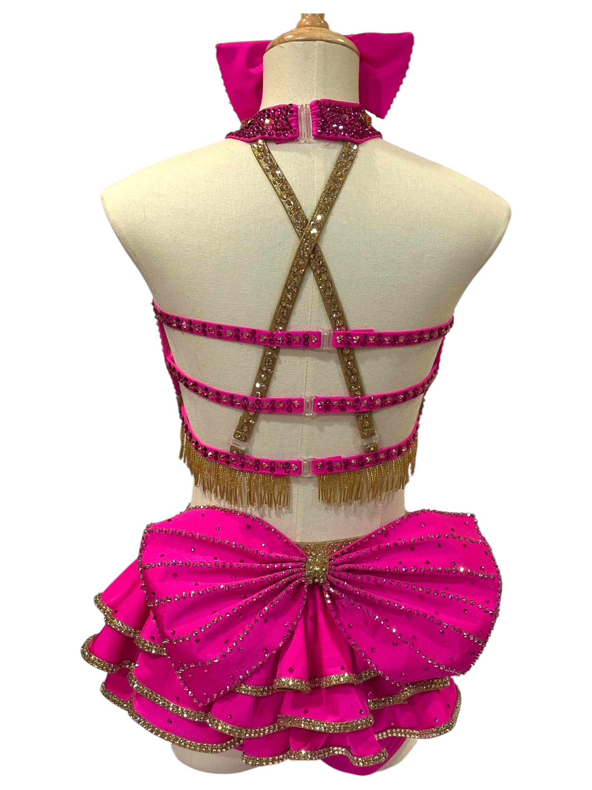 Back view of hot pink and gold dance costume showcasing strappy construction, layered skirt accents, and rhinestone detailing.