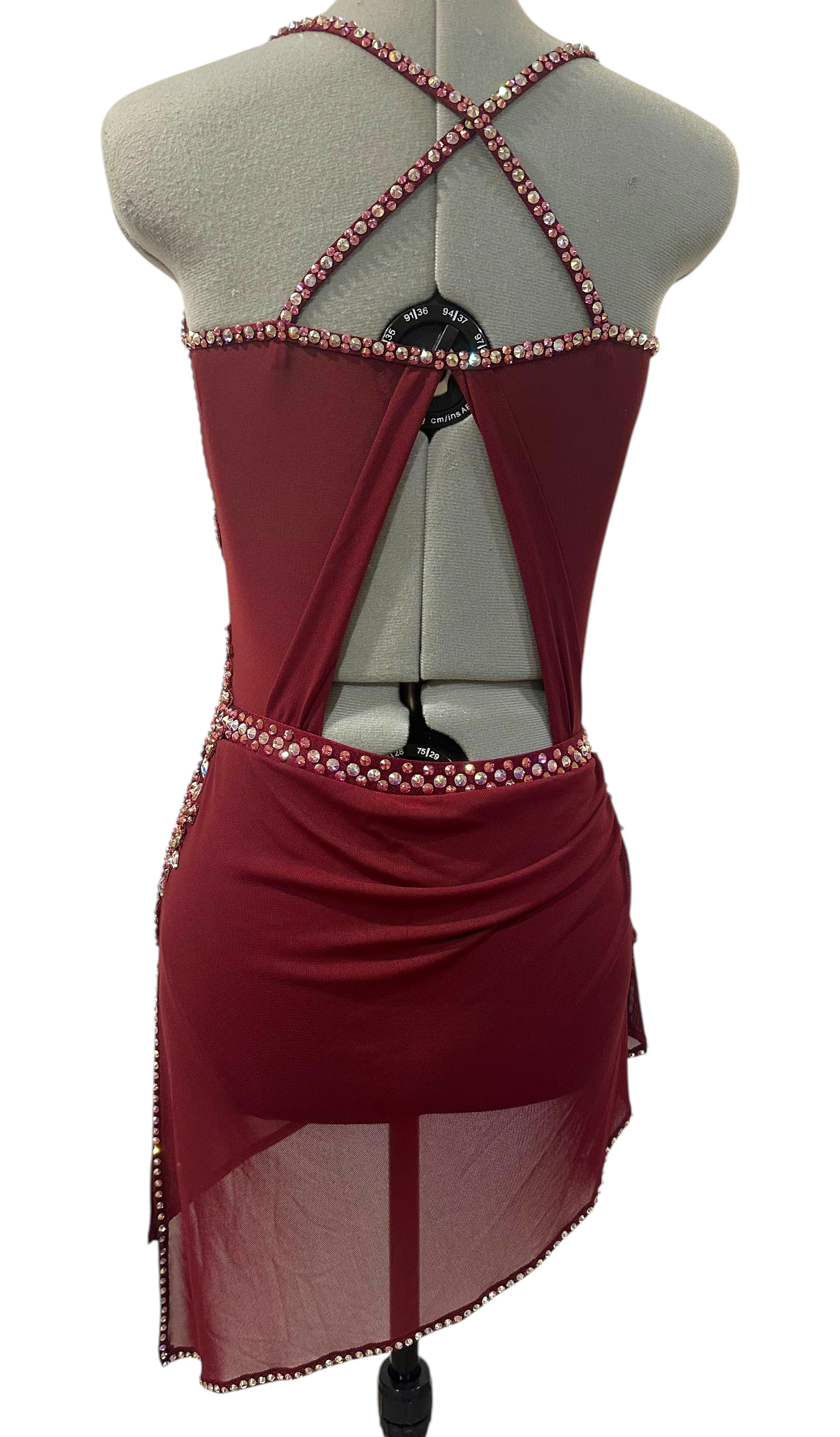 Back view of burgundy competition dance costume featuring crossed rhinestone straps, open back design, and asymmetrical skirt