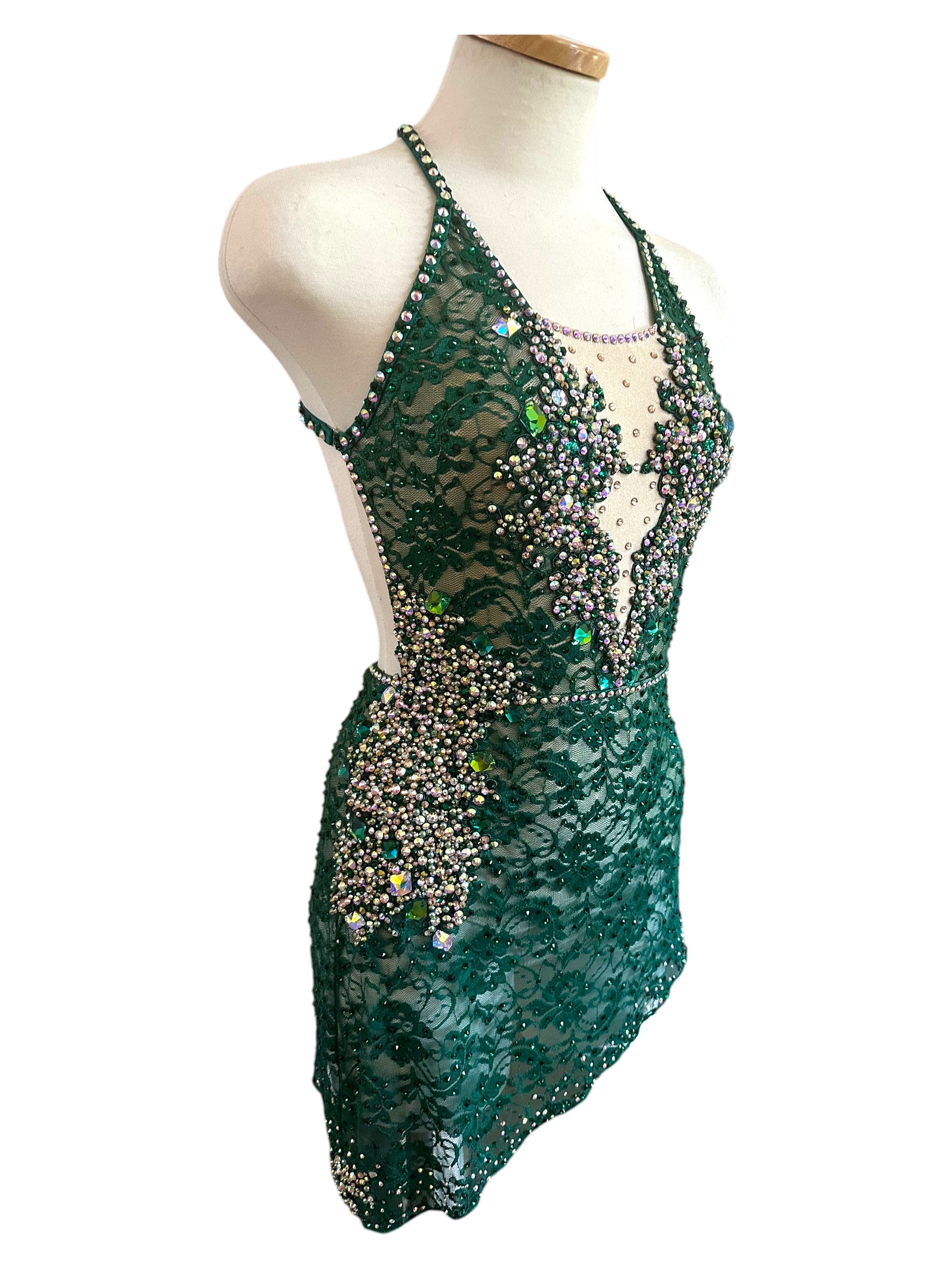 Angled view of emerald green lace dance costume featuring nude illusion plunge neckline and premium rhinestone embellishments