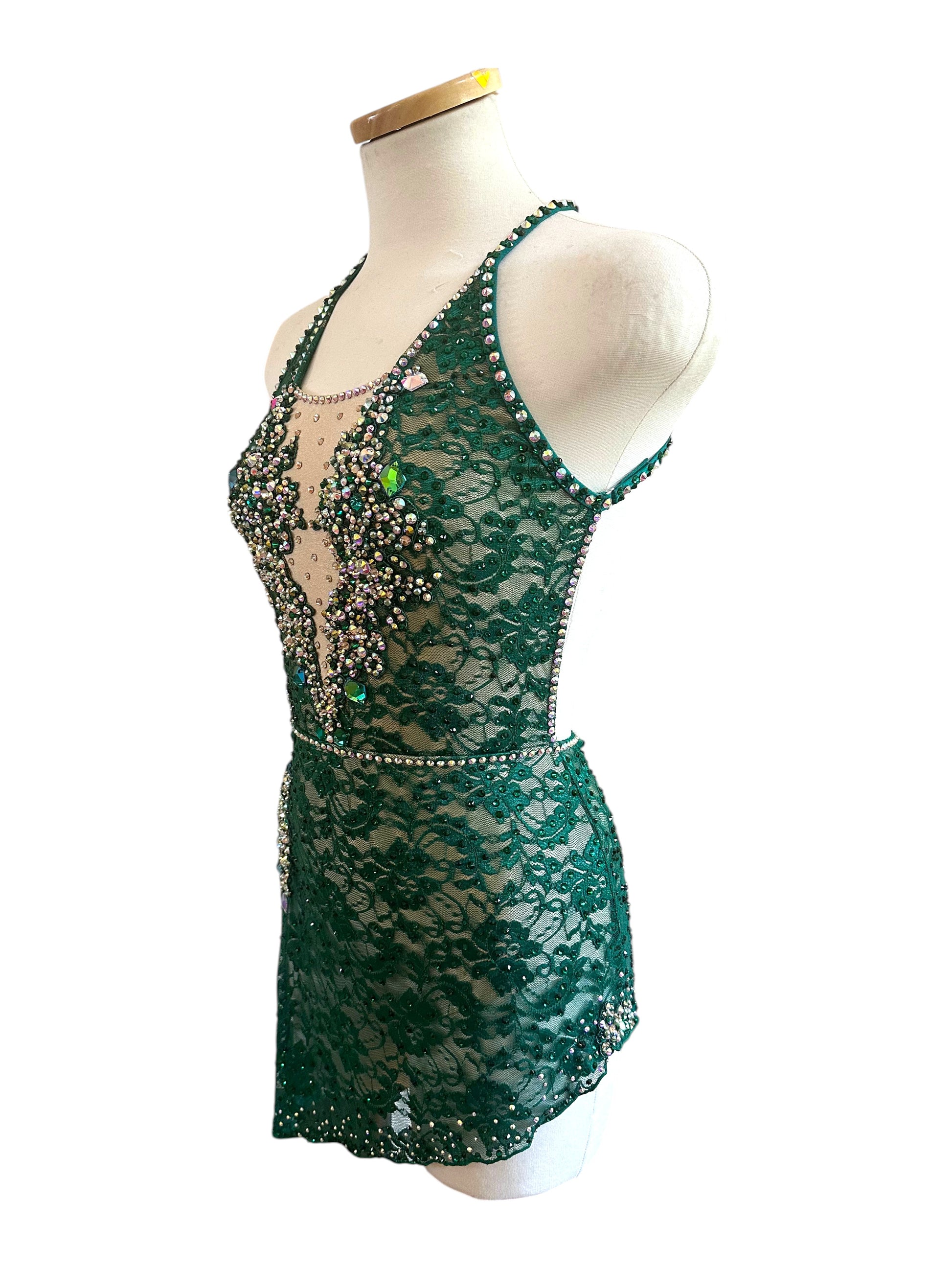Side view of emerald green competition dance costume with rhinestone detailing, lace overlay, and asymmetrical skirt